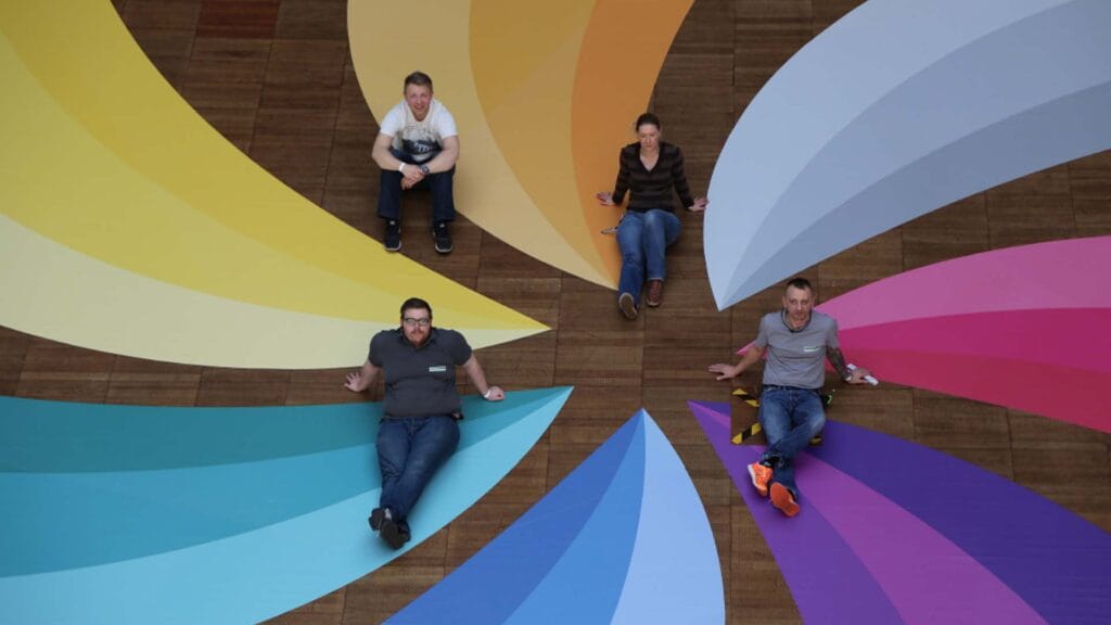 Four Fotoreklame employees sit on a glued-on floor graphic for Telekom.