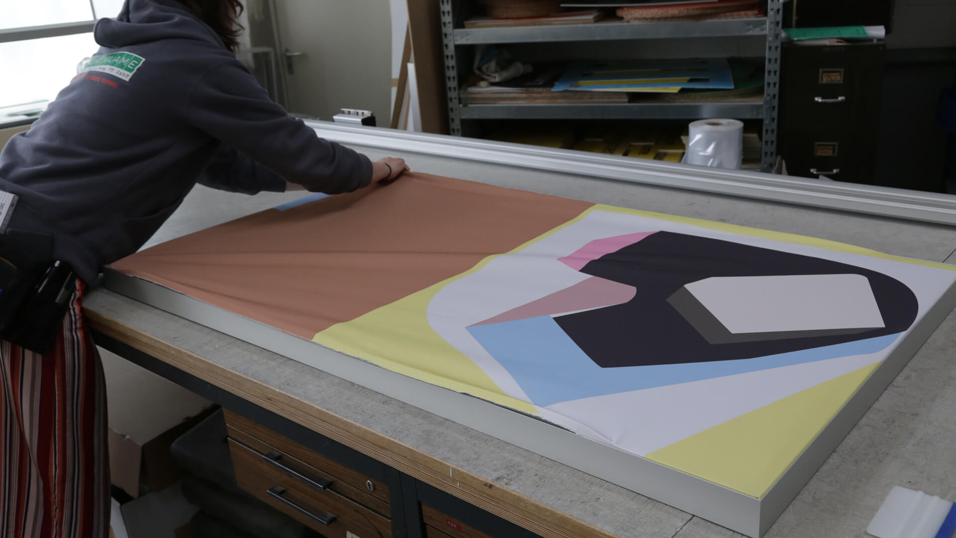 Textiles on walls. A textile tension frame is being fitted with fabric by a staff member from the photo advertising company.